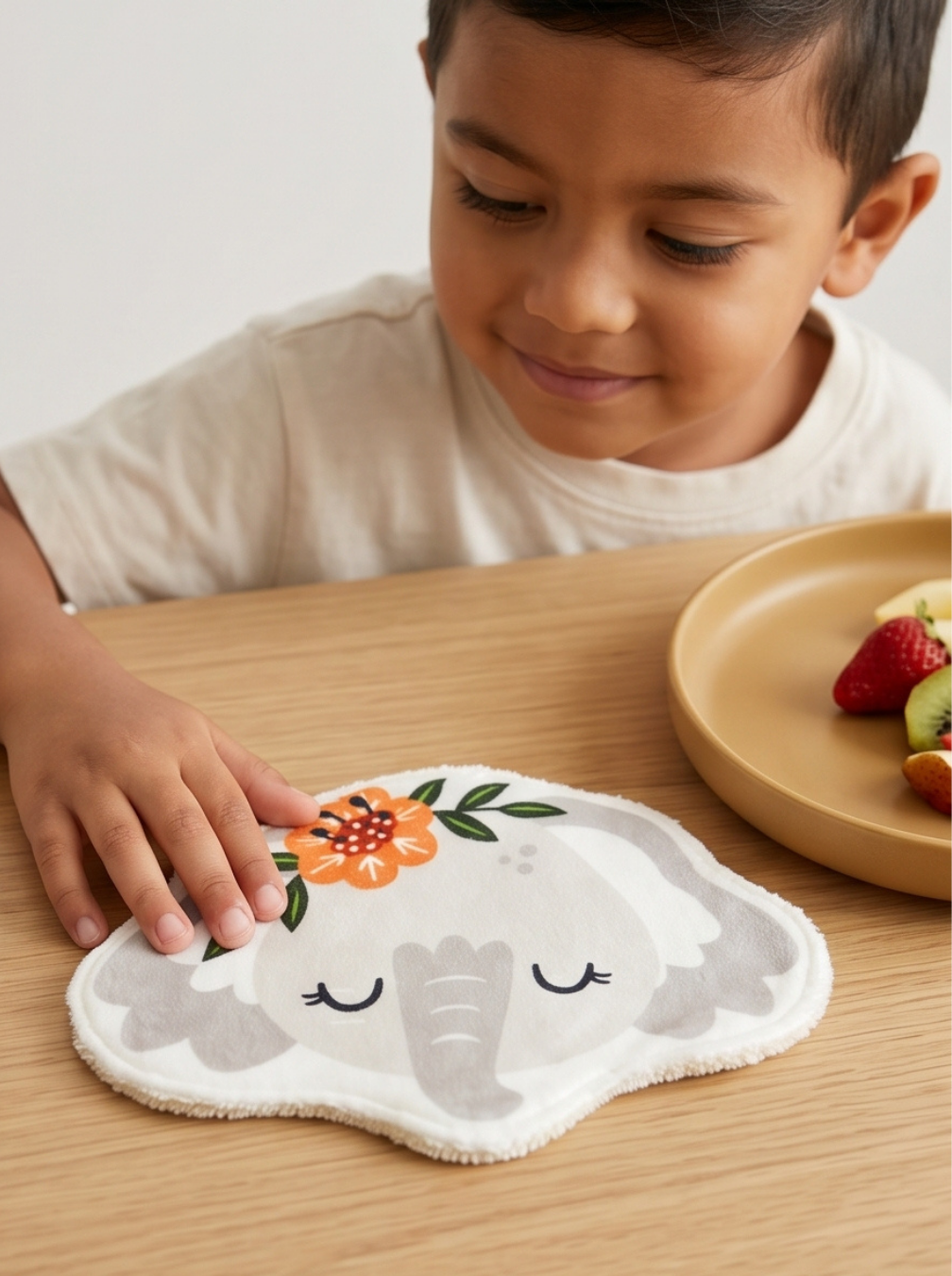 Enfant souriant à table à côté de son coton lavable éléphant de Maison Liaminou. Idée de cadeau de naissance écoresponsable fabriqué en France.