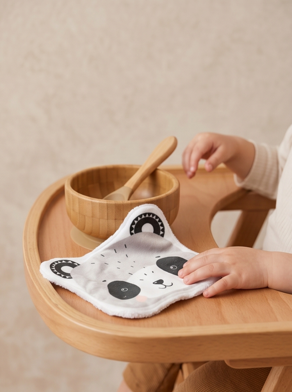 Grand coton lavable en forme de panda posé sur la tablette d'une chaise haute en bois. Lingette lavable bébé en éponge de bambou pour le débarbouillage après le repas.