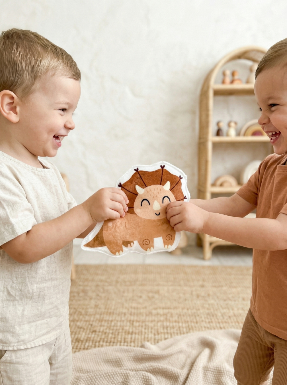 Deux enfants complices s'amusant avec un coton lavable en forme de tricératops de l'Atelier Liaminou. Idée de cadeau de naissance original et durable fabriqué en France.