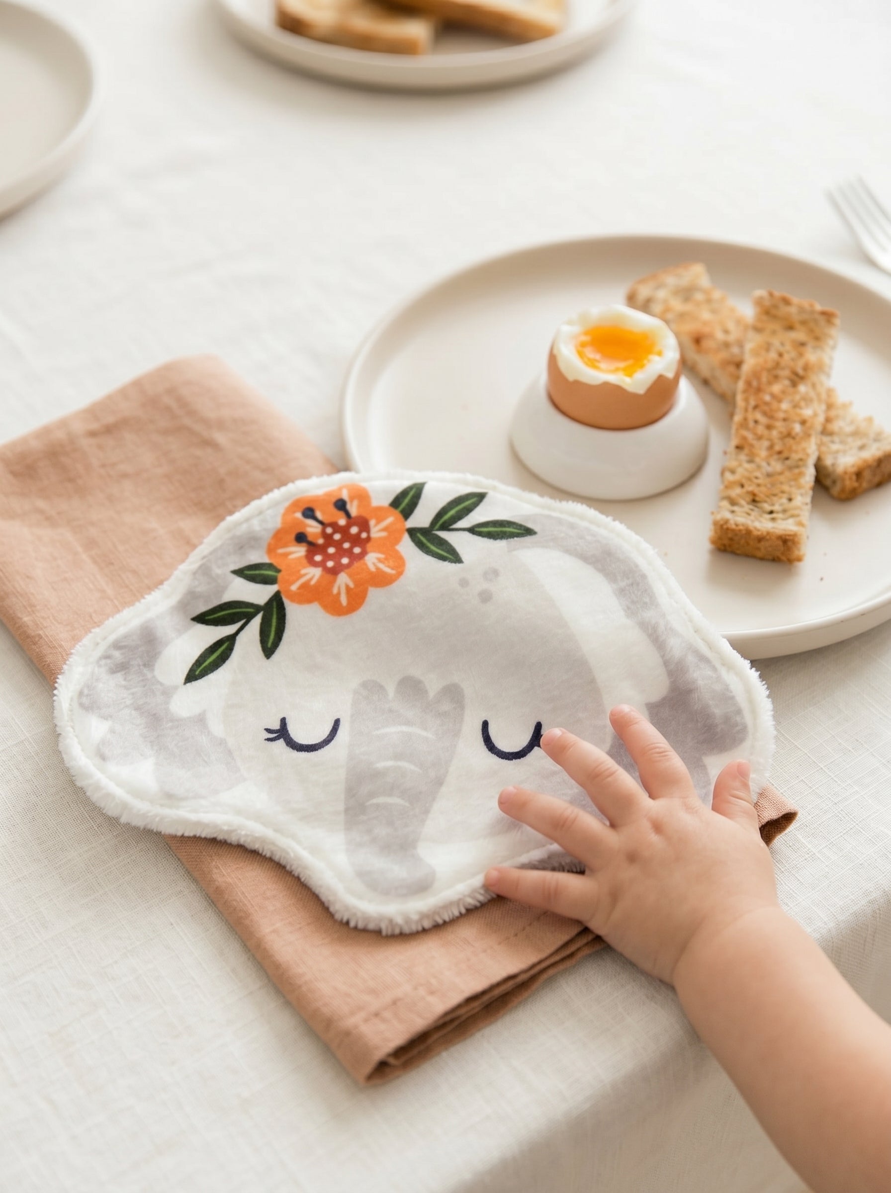 Grand coton lavable en forme d'éléphant avec couronne de fleurs posé sur une table de petit-déjeuner. Lingette lavable bébé artisanale et réutilisable pour débarbouiller les enfants.